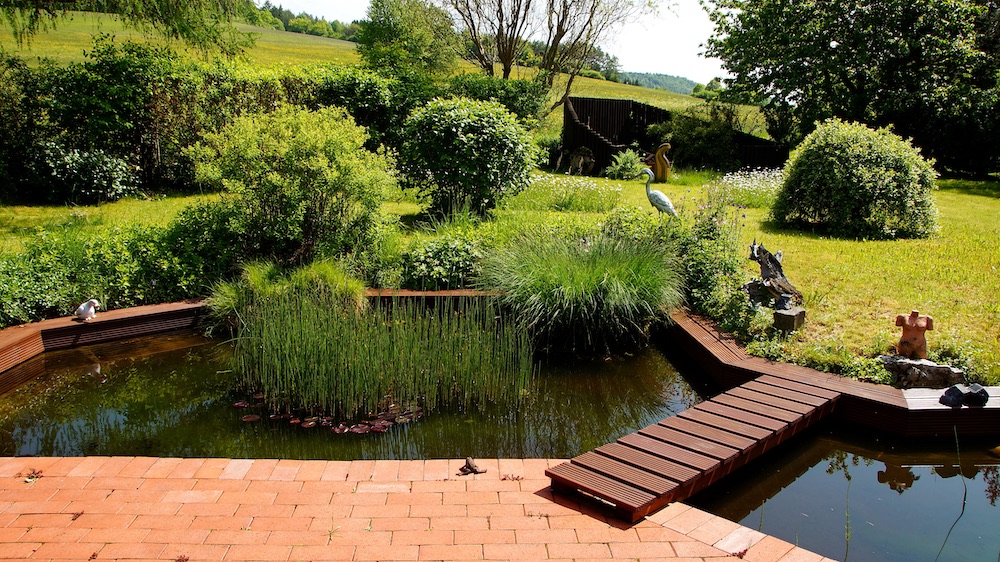attraktiver naturbelassener Garten mit an Terrasse angrenzenden Teich im Frühling